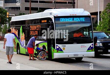 Baltimore, Maryland - Julhy 24, 2013:   Man helps a young boy seated in a wheelchair to board an Orange Route free circulator bus on Pratt Street Stock Photo