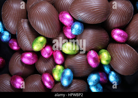 Pile of foil wrapped & unwrapped chocolate easter eggs in pink, blue & lime green. Stock Photo