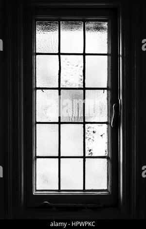 Black and white image of a multi-panelled frosted glass window taken from the inside, with dark surround Stock Photo