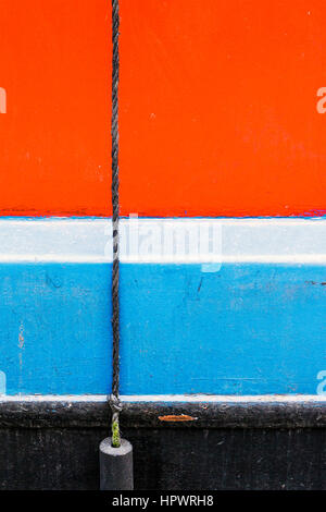 Red, white and blue horizontal stripes on the painted hull of a canal narrowboat with a vertical rope and fender Stock Photo