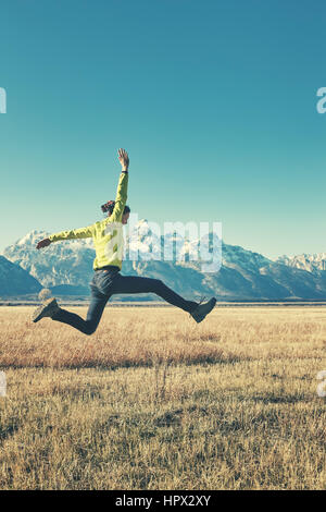 Retro stylized picture of a happy young woman jumping on a mountain meadow, Grand Teton National Park, Wyoming, USA. Stock Photo