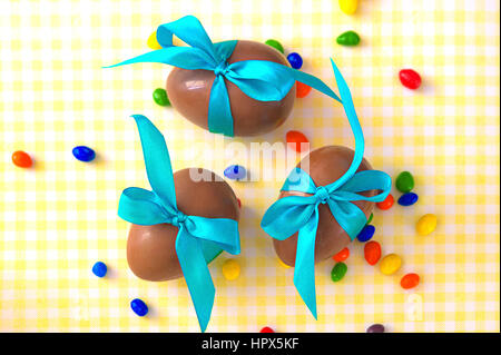Chocolate Easter eggs over yellow tablecloth with turquoise ribbon bow Stock Photo