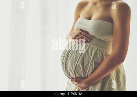 Young beautiful pregnant woman standing near window at home Stock Photo