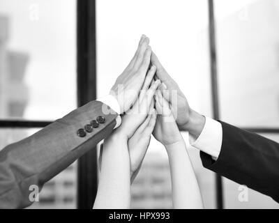 businesspeople putting hands together to form a pyramid in a display of team spirit and determination, black and white. Stock Photo