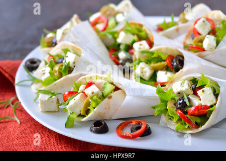 Mini tortillas stuffed with Greek farmers salad with feta cheese and olives, served in white paper bags