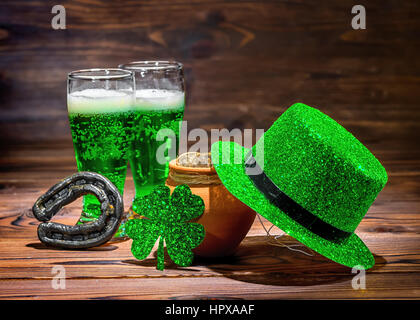 St Patricks day with glasses of green beer, leaf clover, leprechaun hat, horseshoe and pot full gold coins on vintage wooden background, close up Stock Photo