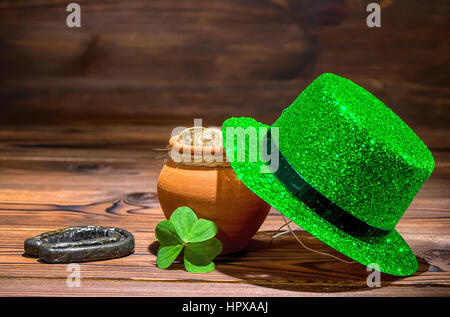 St Patricks day concept with pot full gold coins, horseshoe, green hat and shamrock on vintage wooden background, close up Stock Photo