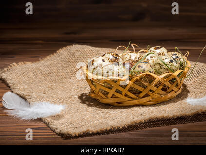 quail eggs with straw and feathers in basket on sackcloth, rural style, close up Stock Photo