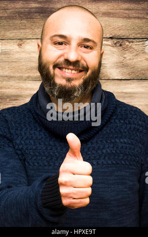 Handsome, bald man with beard  with her thumb up in sign of optimism  on a wooden background Stock Photo