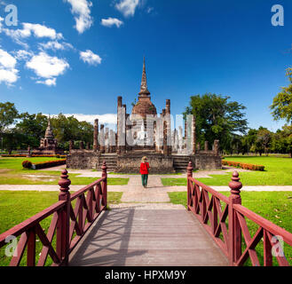 Tourist Woman in red costume looking at ancient Buddha statue in Wat Sa Si of Sukhothai Historical Park, Thailand Stock Photo