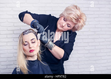 Stylist working with hair. Female hairdresser applying color to customer at hair salon. Portrait of professional hairdresser middle aged woman colorin Stock Photo