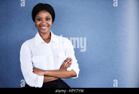 Young black female business executive smiling at camera with her arms crossed while smiling at the camera and standing against a textured blue backgro Stock Photo