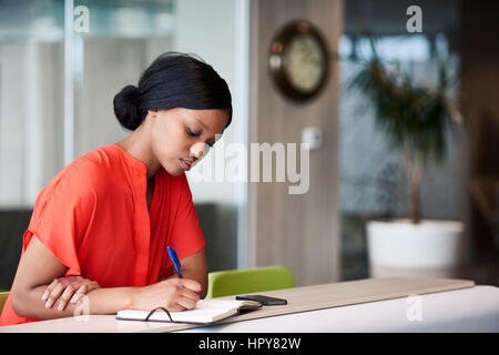Authentic image of African American woman busy using a pen to write down her shedule that she has planned out in her notebook while sitting in the col Stock Photo