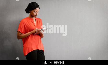 Young black businesswoman busy using the digital tablet that she is holding in her hands to conduct business remotely making use of the internet. Stock Photo