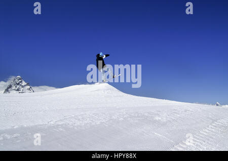 Snowboarder jump in terrain park at ski resort on sun winter day. Caucasus Mountains, region Dombay. Stock Photo