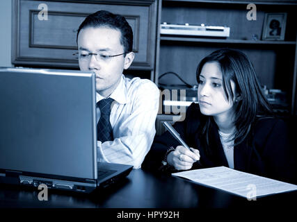 business partners on a laptop in an office taking notes - blue tint Stock Photo