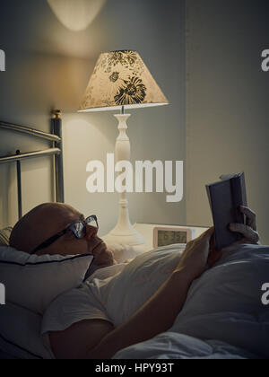 Middle aged man reading Bible on bed Stock Photo