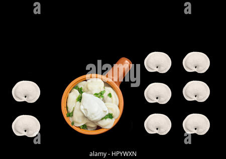 Dumplings with greens and sour cream in a ceramic bowl isolated on black background. bit, top view. Stock Photo