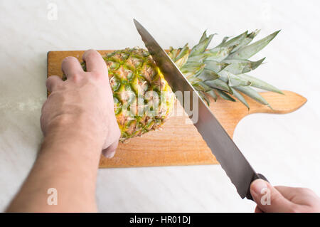 Hands cutting  fresh pineapple on a wooden board Stock Photo