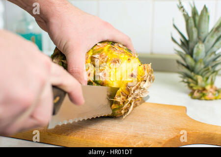 Hands cutting  fresh pineapple on a wooden board Stock Photo