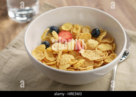berries falling into corn flakes for breakfast in bowl on table, breakfast preparation Stock Photo