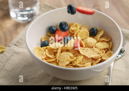 berries falling into corn flakes for breakfast in bowl on table, breakfast preparation Stock Photo