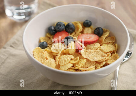 berries falling into corn flakes for breakfast in bowl on table, breakfast preparation Stock Photo