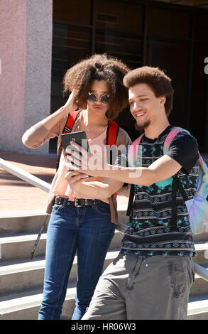 A young woman and man with books and electronics on a college campus. Stock Photo