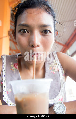 Portrait of a girl drinking iced coffee in a outdoors restaurant. Cheerful woman drinking a beverage from a plastic cup with a straw. Stock Photo
