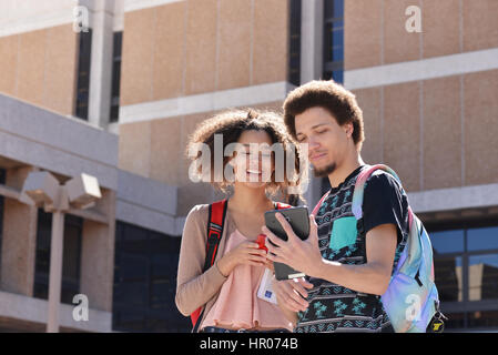 A young woman and man with books and electronics on a college campus. Stock Photo