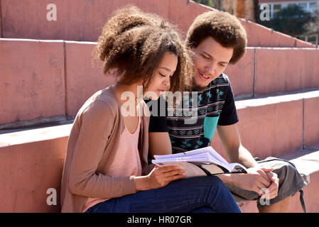 A young woman and man with books and electronics on a college campus. Stock Photo