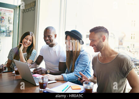 Four young so-workers at desktop using laptop and smiling in light spacious modern office. Stock Photo