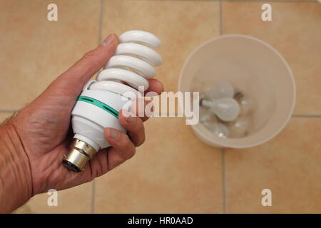 Holding a low energy CFL light bulb with discarded tungsten bulbs in background Stock Photo