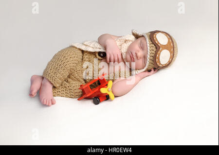 Sleeping two week old newborn baby boy wearing an aviator hat and outfit.
