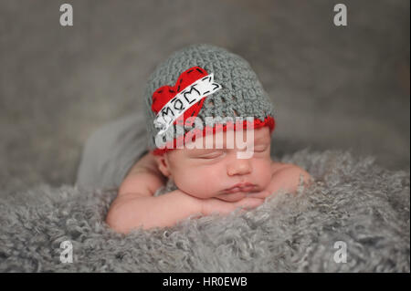 Two week old sleeping, baby boy wearing a crocheted 'Love Mom' beanie. He is sleeping on gray sheepskin. Stock Photo
