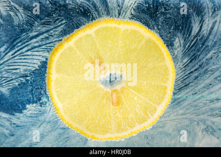 Slice of yellow lemon with seeds in water with bubbles on the background of a frosty pattern Stock Photo
