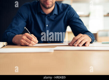 Closeup of a successful young businessman writing on documents while sitting at a table in an office Stock Photo