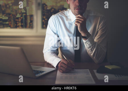 Cropped portrait of businessman sitting at desk at night working overtime Stock Photo