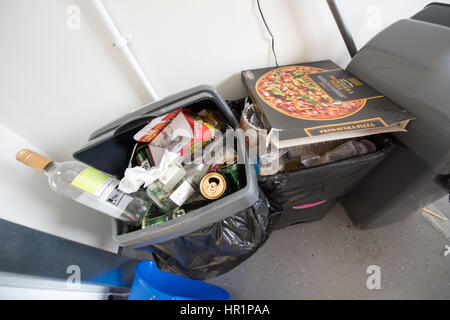 Overflowing dirty kitchen plastic swing bins full of rubbish, pizza boxes, wine bottles and beer cans in a student hall of residence communal kitchen Stock Photo
