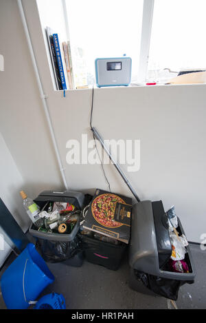 Overflowing dirty kitchen plastic swing bins full of rubbish, pizza boxes, wine bottles and beer cans in a student hall of residence communal kitchen Stock Photo