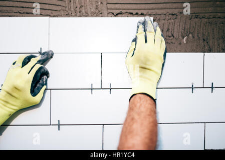 industrial worker hands installing ceramic tiles on interior walls, handyman using plastic distancer for adjusting tiles. Construction details Stock Photo