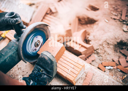 Industrial worker cutting through bricks. Professional brickmason using grinder at building houses Stock Photo