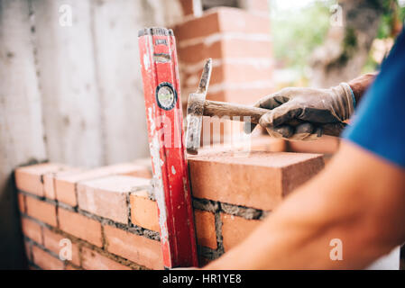 industrial worker building exterior walls, using hammer and level for laying bricks in cement. Detail of worker with tools Stock Photo