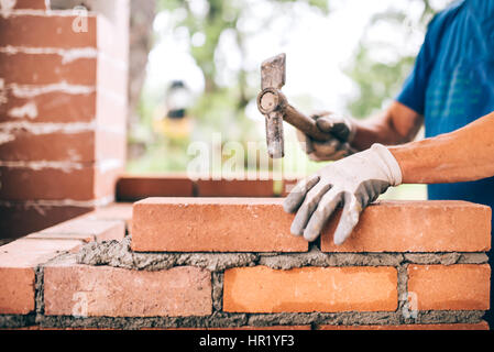 industrial worker building exterior walls, using hammer for laying bricks in cement. Detail of worker with tools Stock Photo