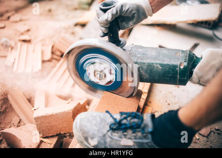 worker using grinder on construction site for cutting bricks, debris. Tools and bricks on new building site Stock Photo