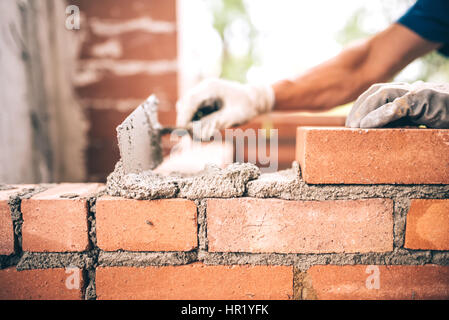 Bricklayer worker installing brick masonry on exterior wall with trowel putty knife Stock Photo