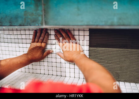 Close up of handyman hands fixing and applying ceramic tiles on bathroom walls. Stock Photo