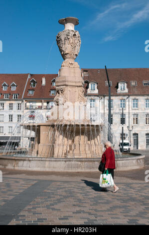 Woman with red coat walks past fountain monument in Place de la Revolution Besancon France Stock Photo