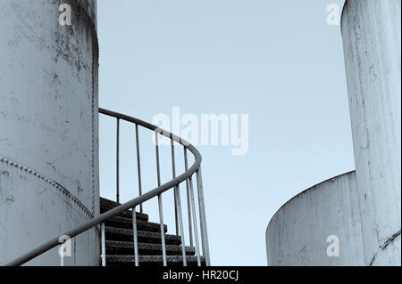 Steps with rusty railing going up out of site along the side of a storage/holding tank in an industrial area Stock Photo