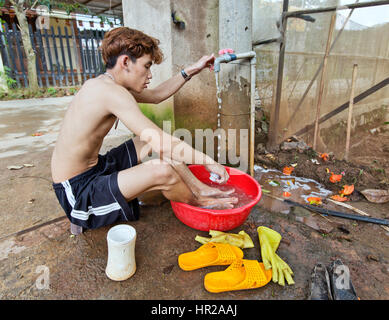 Young man cleaning up , washing his feet, after planting tomato seedlings in tunnel. Stock Photo